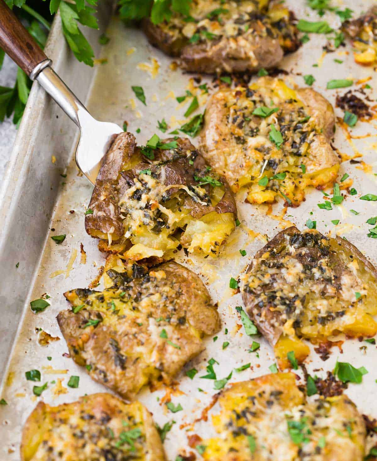 Crispy smashed potatoes on a sheet pan, sprinkled with parmesan and fresh parsley.