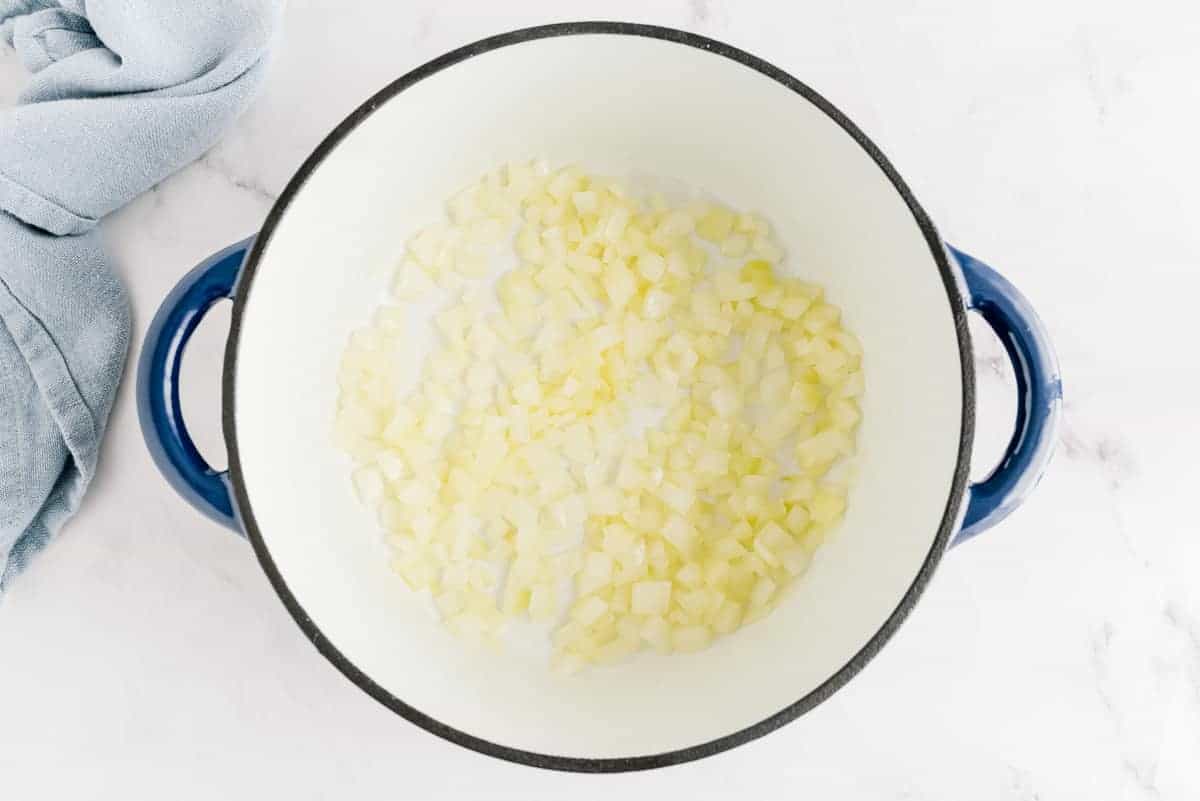 Onions cooking in oil in a blue and white pot.