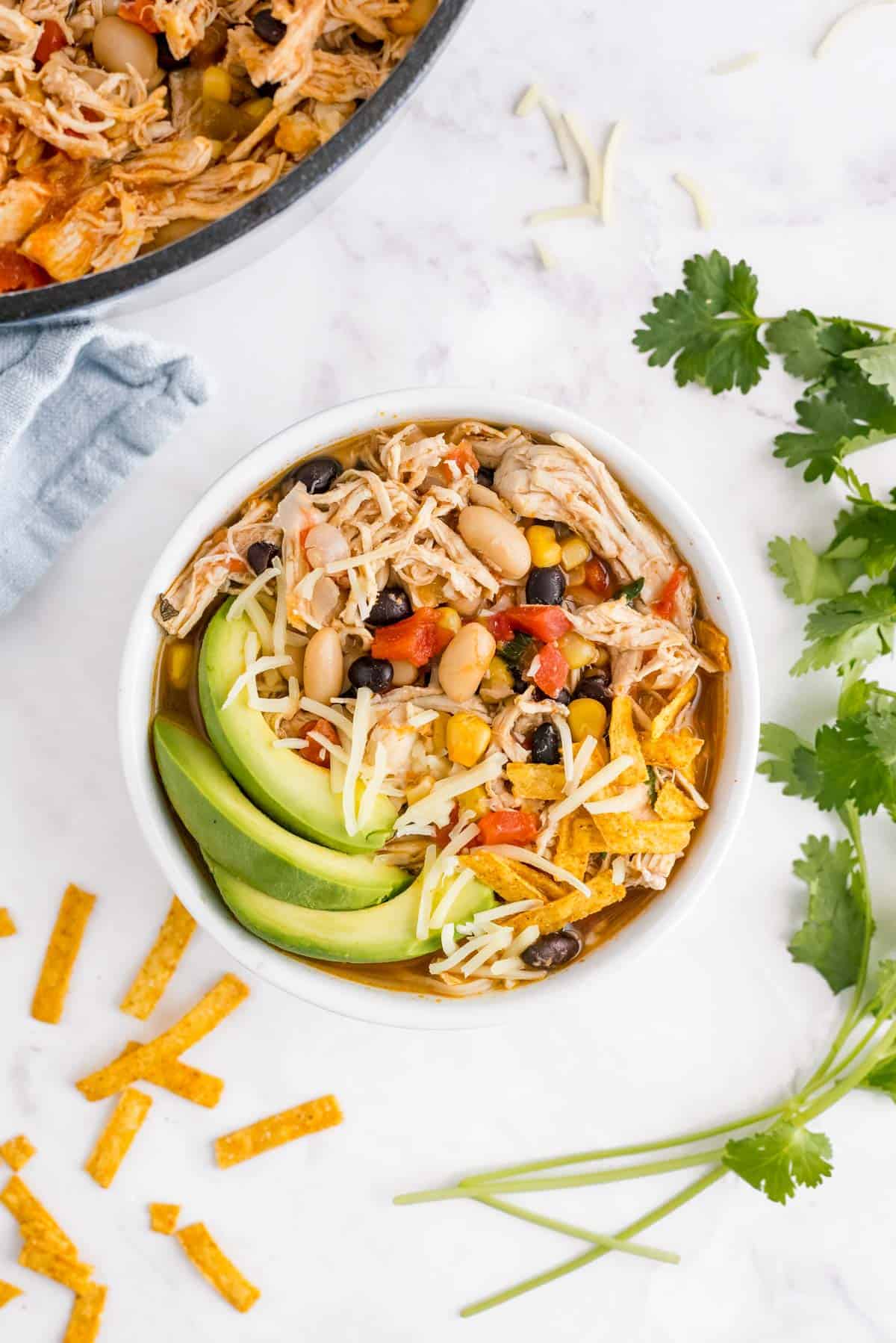 Chicken chili in a bowl with avocados, cilantro, and cheese.