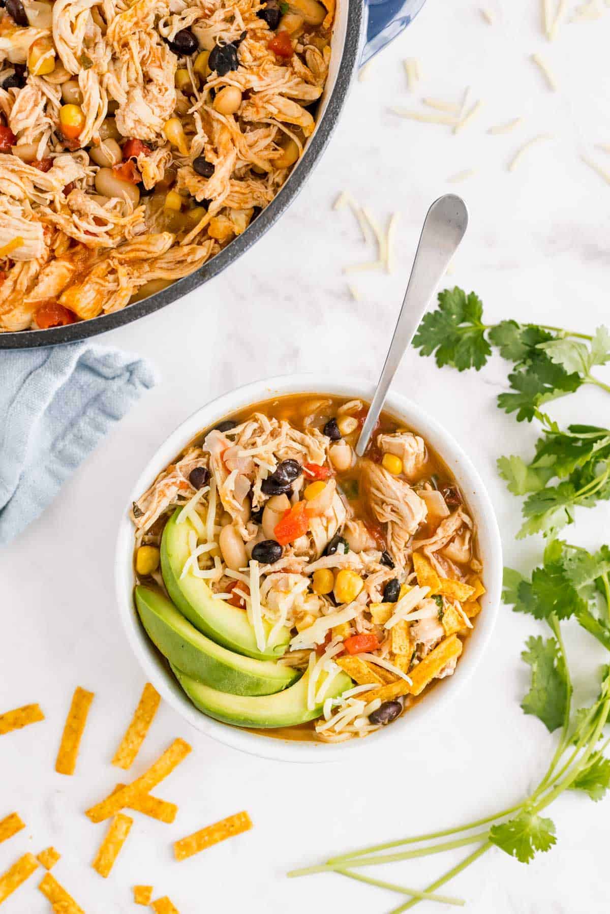 White chili in a bowl and in a pot, with fresh cilantro and tortilla strips.