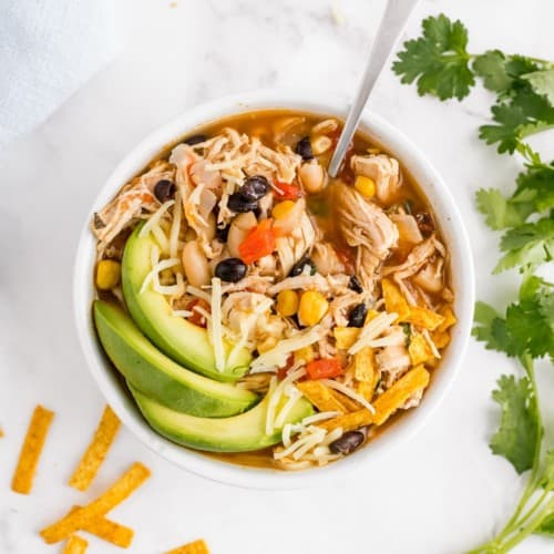 Chicken chili in a bowl garnished with avocado, cilantro, cheese.