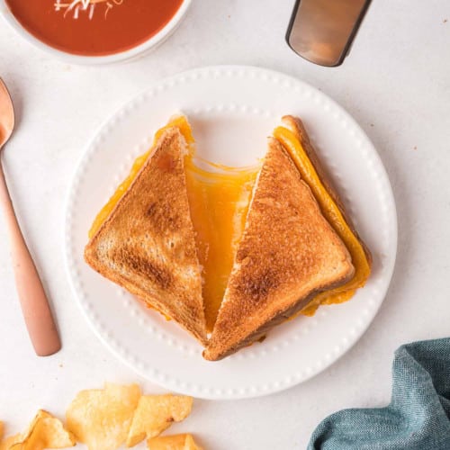 Air fryer grilled cheese sandwich on a white plate, halves pulled apart to show cheese.