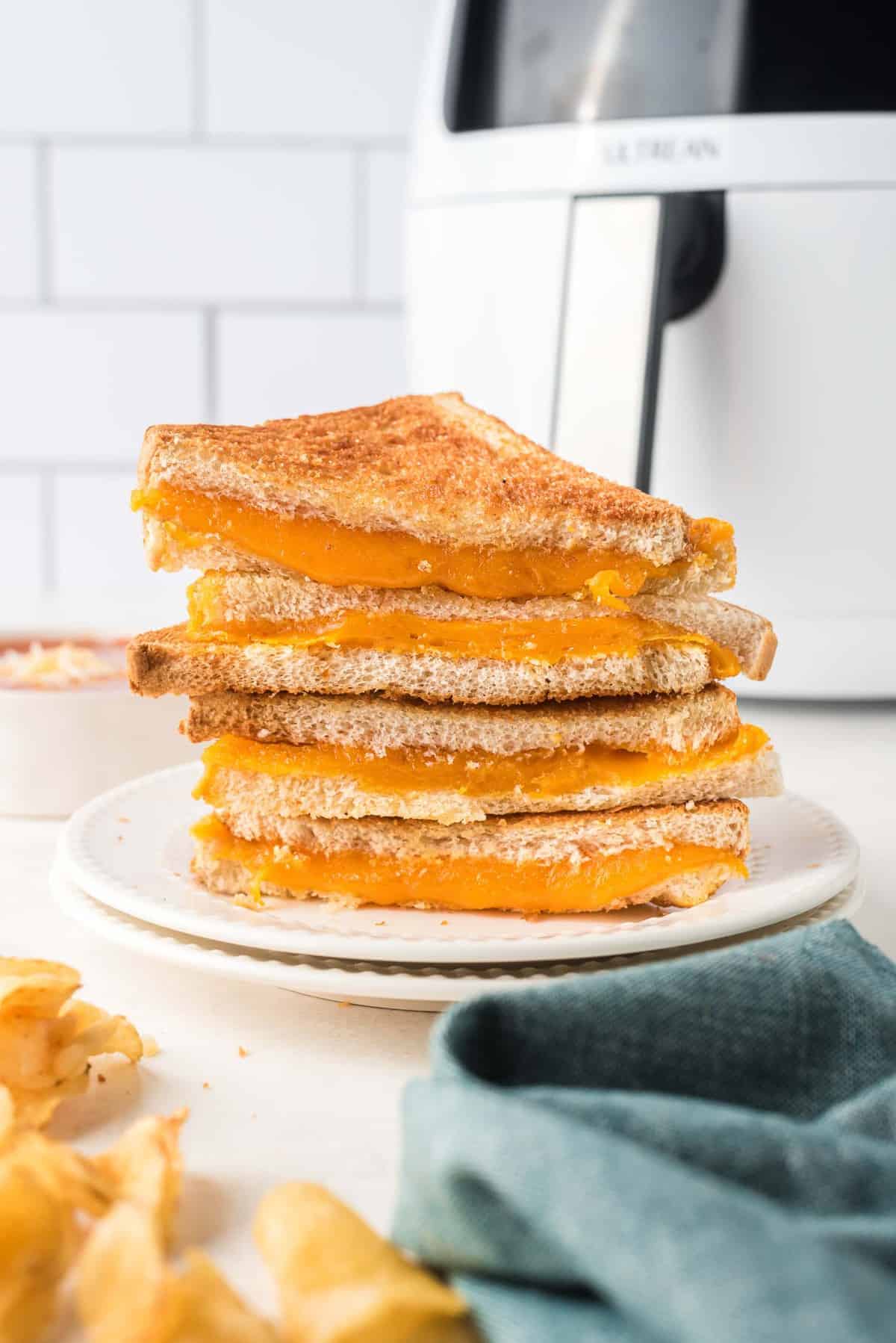 Stack of super cheese grilled cheese sandwich halves, with an air fryer in the background.