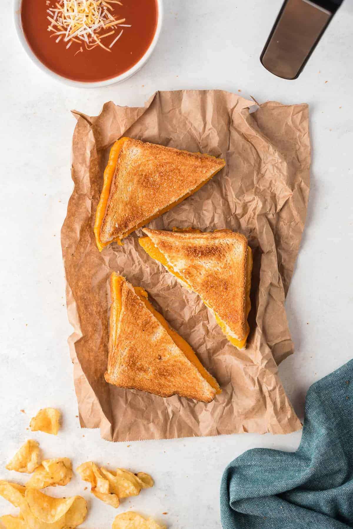 Overhead view of toasted sandwich halves, potato chips, and a bowl of cheese topped tomato soup.