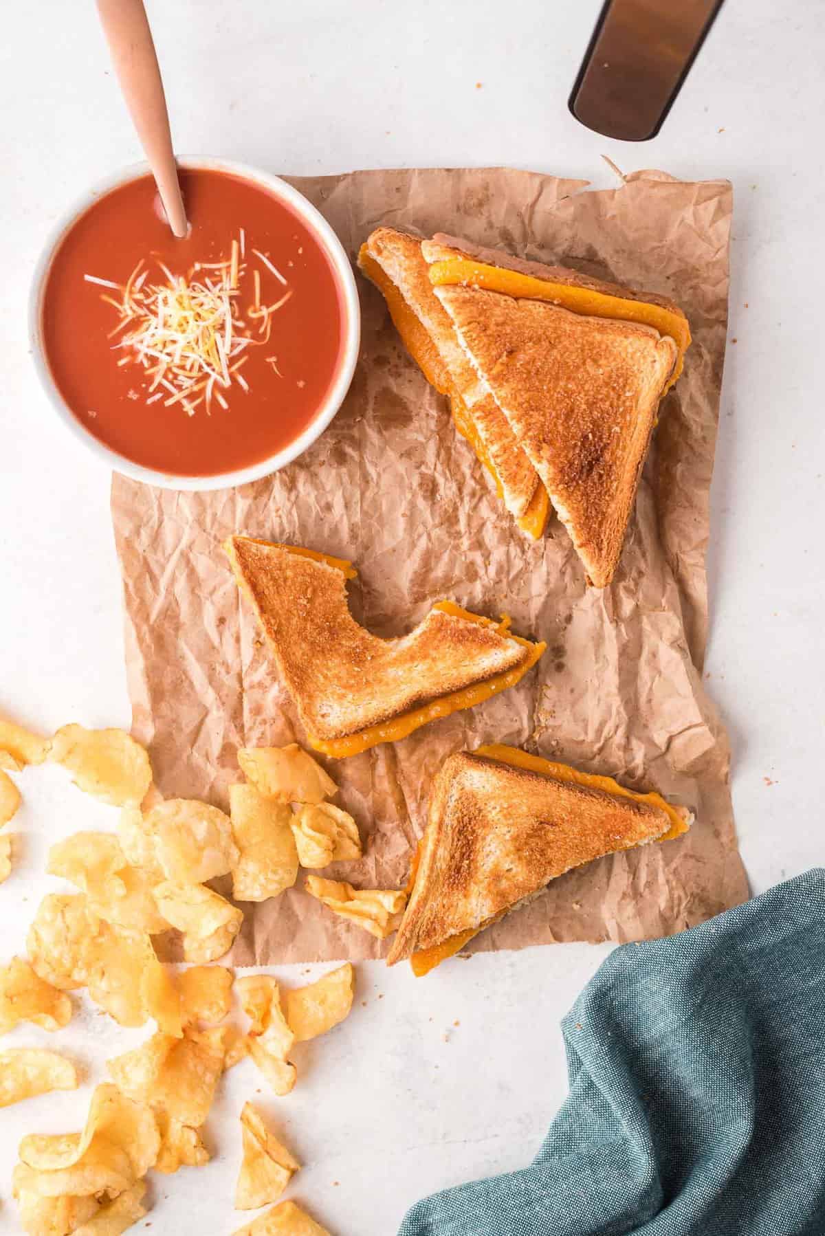 Toasted sandwich with cheese, alongside potato chips and tomato soup.