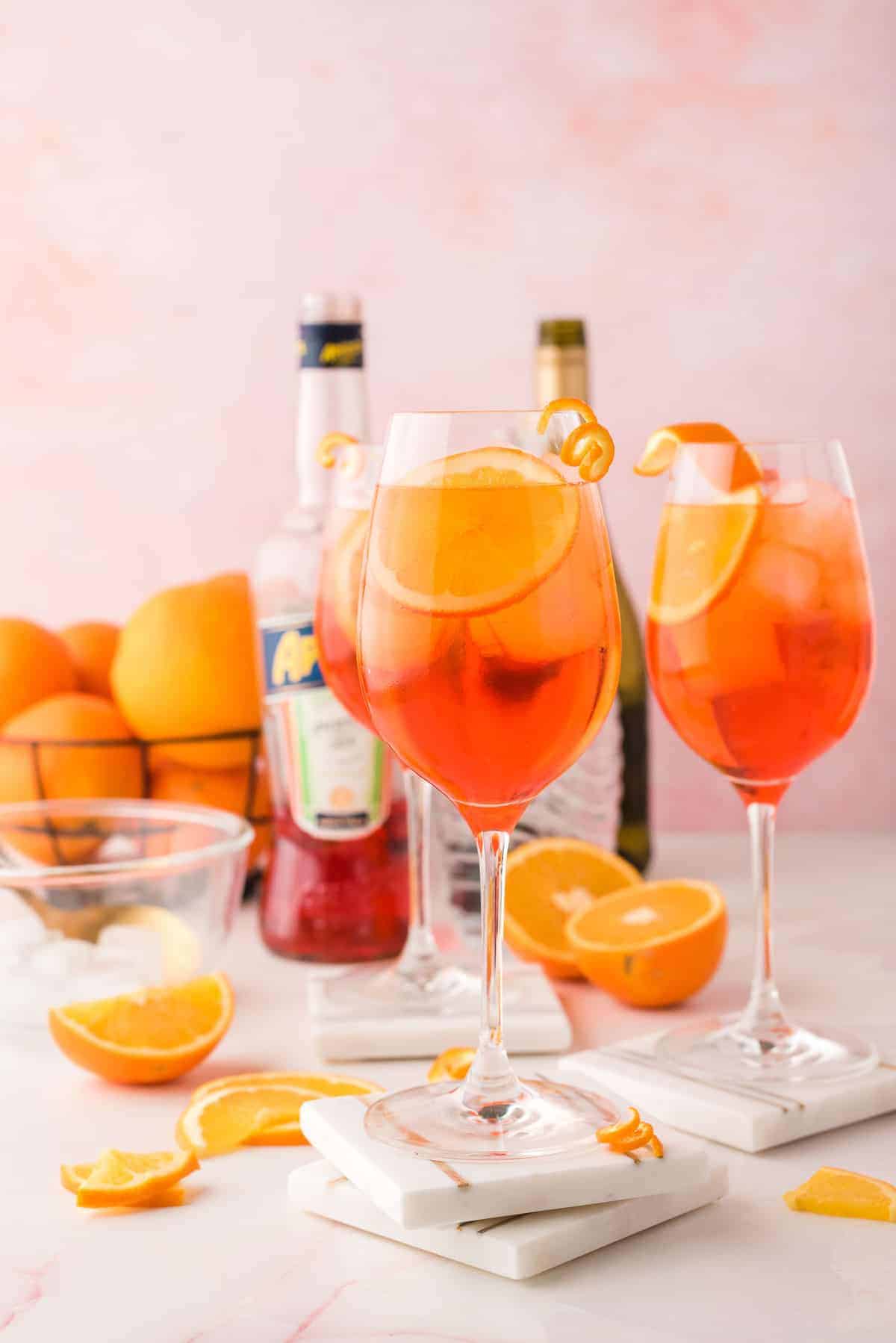 Thre glasses of aperol spritz, with the ingredients need to make it in the background.