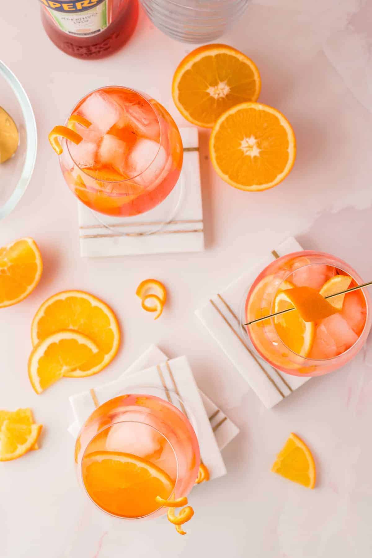 Overhead view of orange-colored drinks over ice, orange slices scattered around.