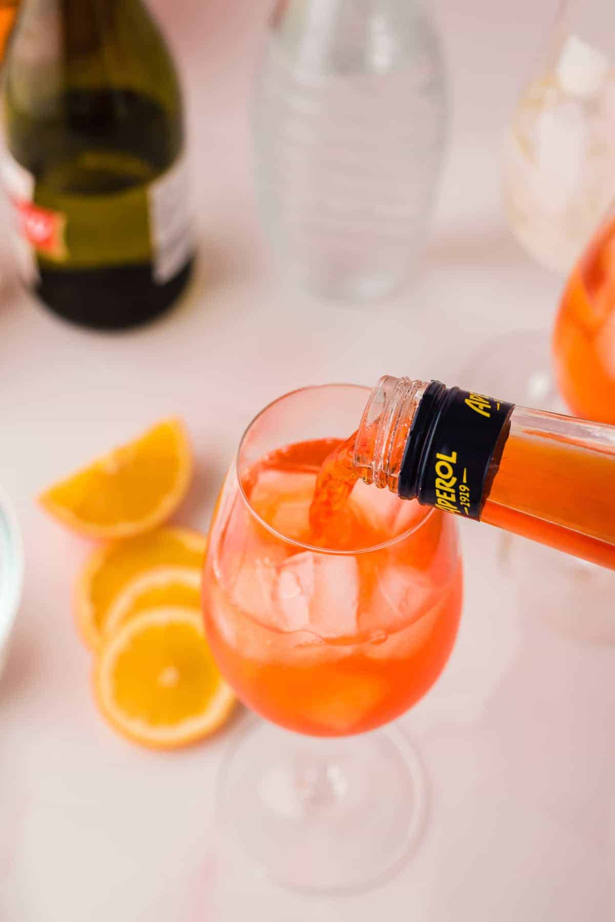 Aperol being poured into a wine glass with ice.