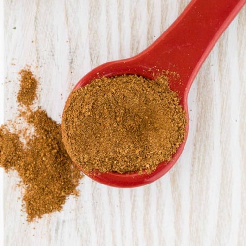 Overhead view of apple pie spice on a red ceramic measuring spoon.