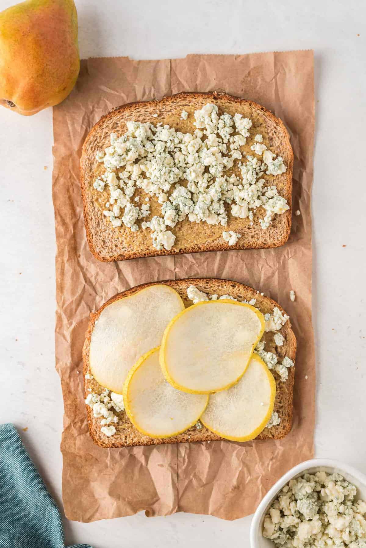 An open faced grilled cheese before it is cooked, containing pears and blue cheese crumbles.