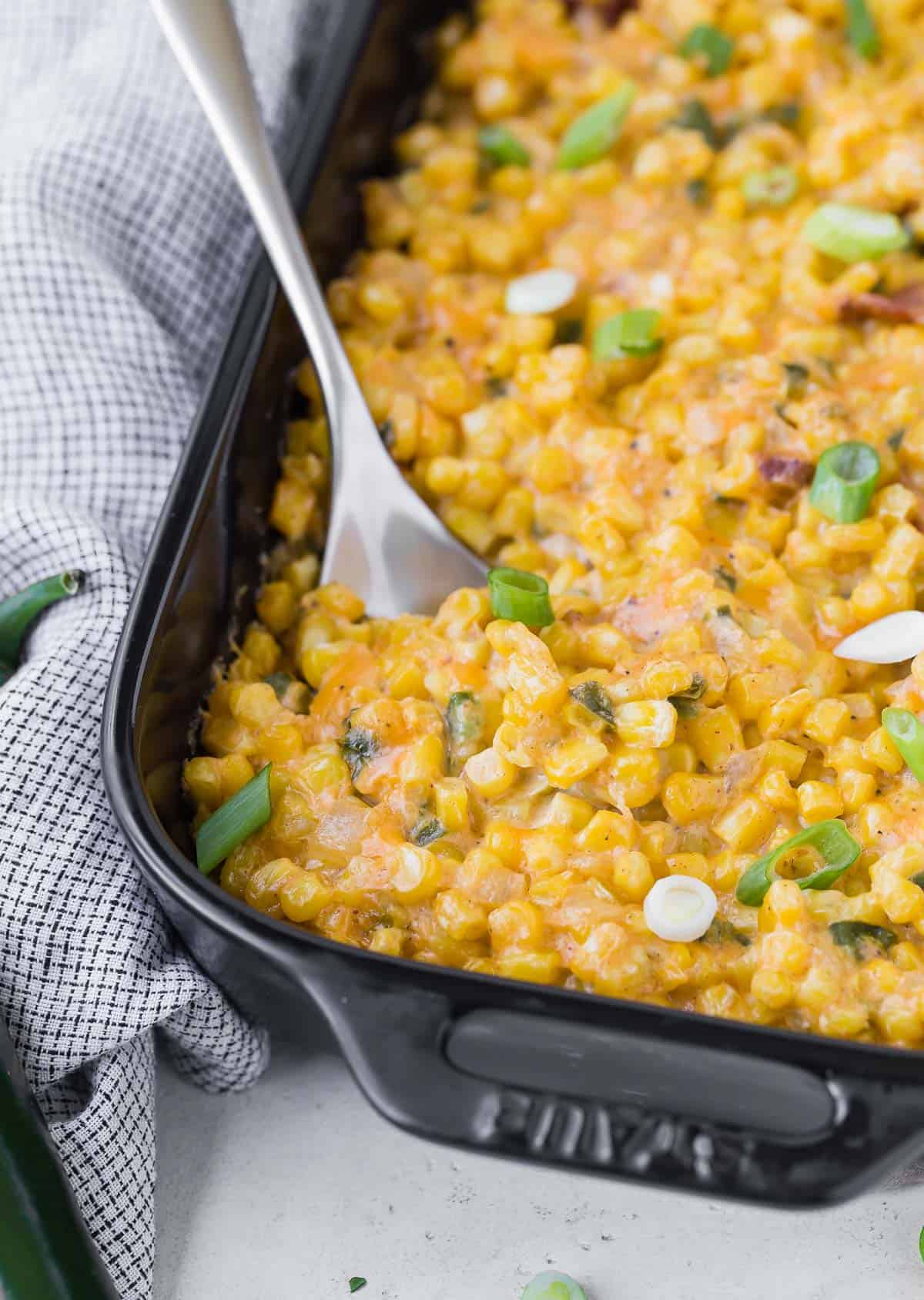 Corn and cheese casserole being scooped out of a black baking dish.