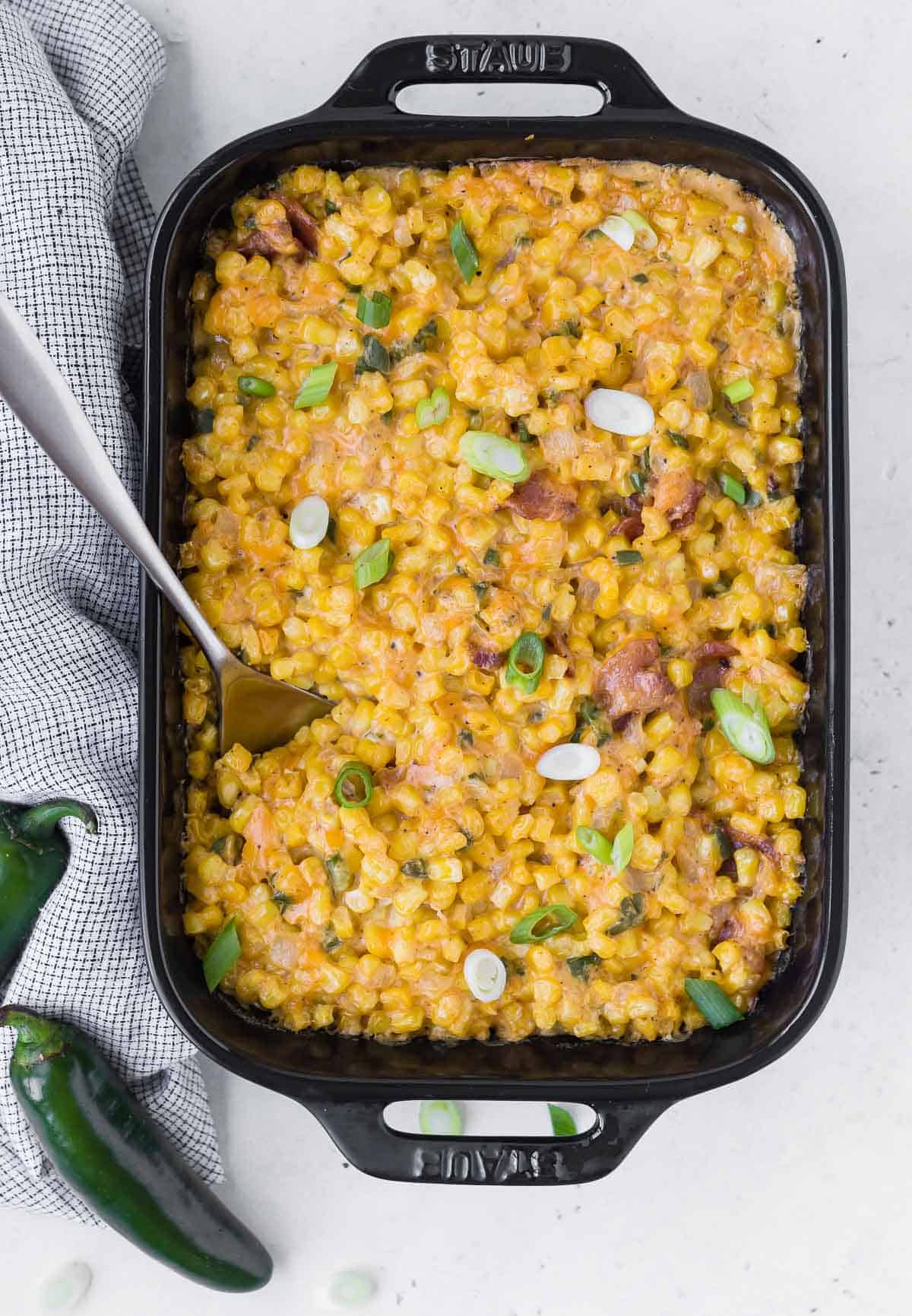 Full overhead view of a black casserole dish filled with cheese, corn, jalapeno, and bacon.