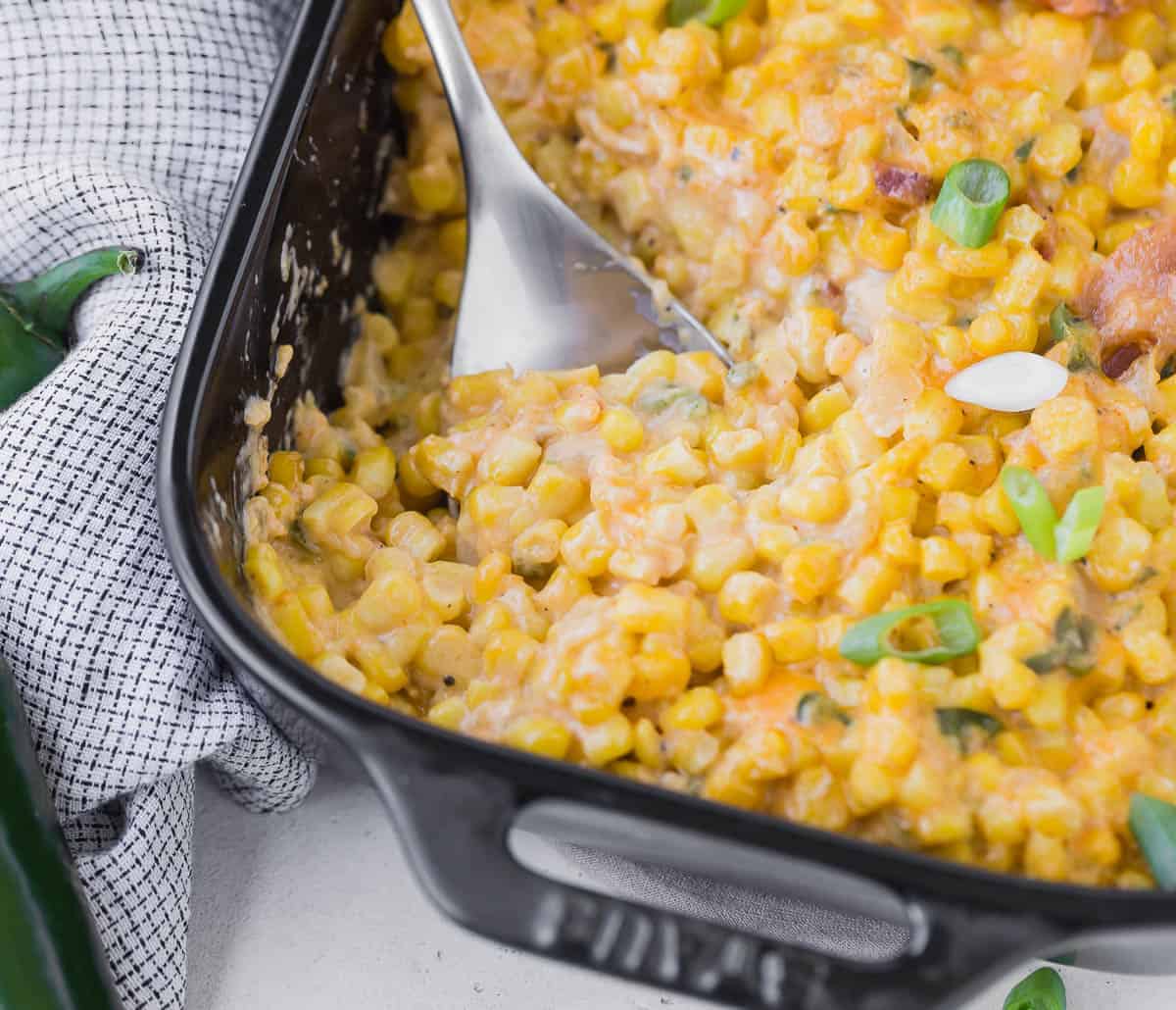 Close up of a casserole made with corn, bacon, and peppers, being scooped out with a spoon.