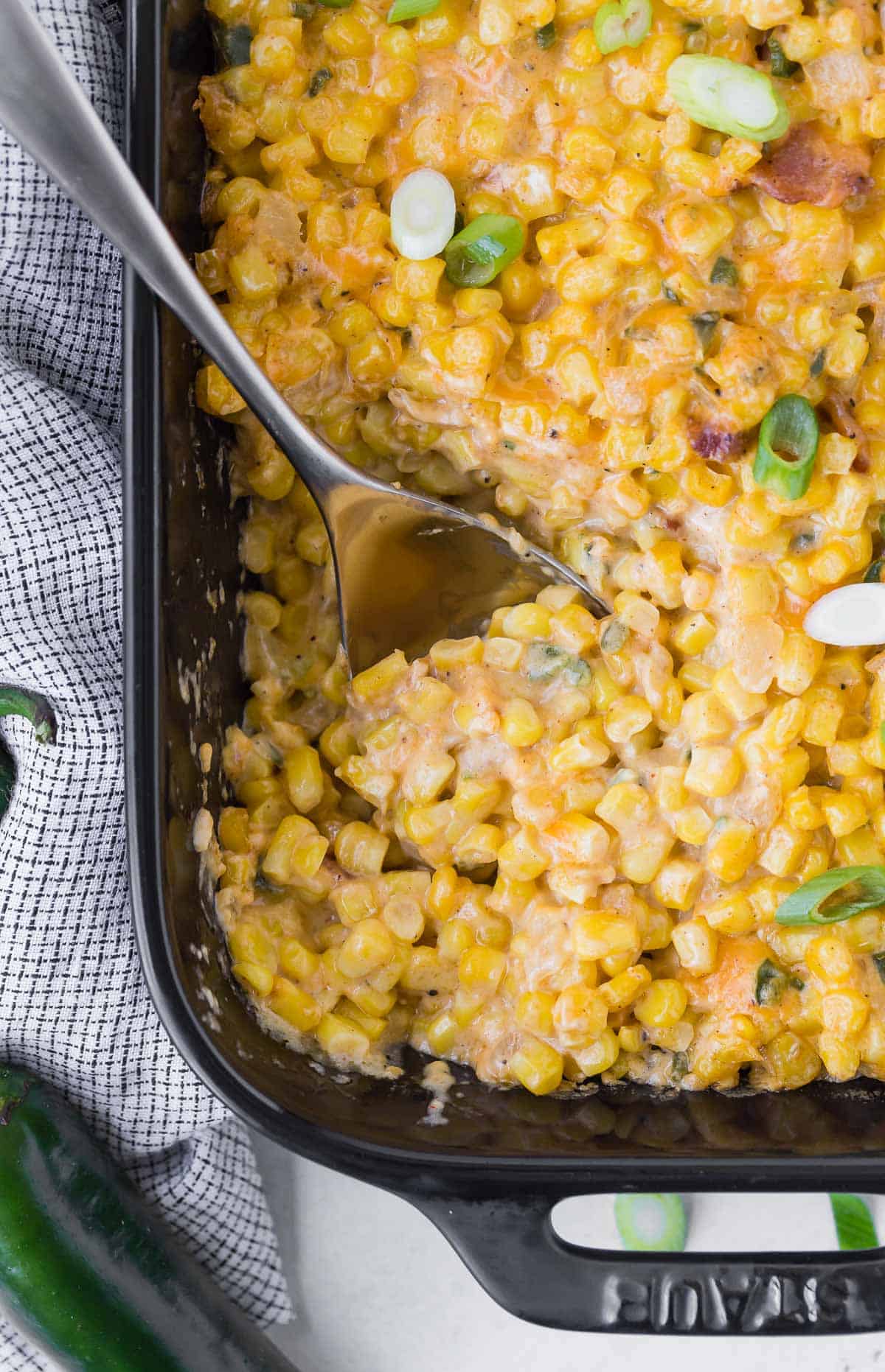 Overhead view of corn casserole in a black baking dish, sprinkled with green onions.