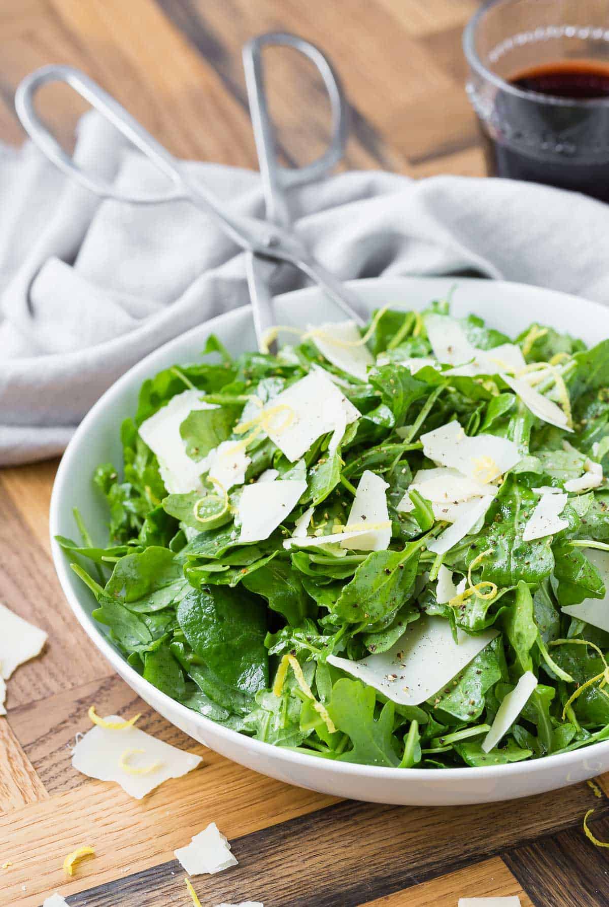 Arugula, parmesan, and lemon zest in a white bowl on a wooden background.