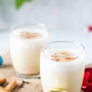 Two glasses of egg nog surrounded by Christmas ornaments.