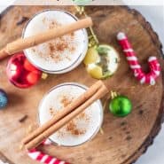 Overhead view of two glasses of egg nog, topped with cinnamon sticks.