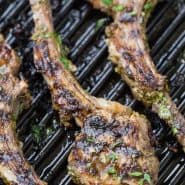 Overhead view of lamb on a grill pan. Text overlay reads "garlic herb grilled lamb chops, rachelcooks.com"