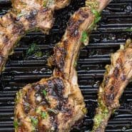 Overhead view of lamb on a grill pan. Text overlay reads "garlic herb grilled lamb chops, rachelcooks.com"