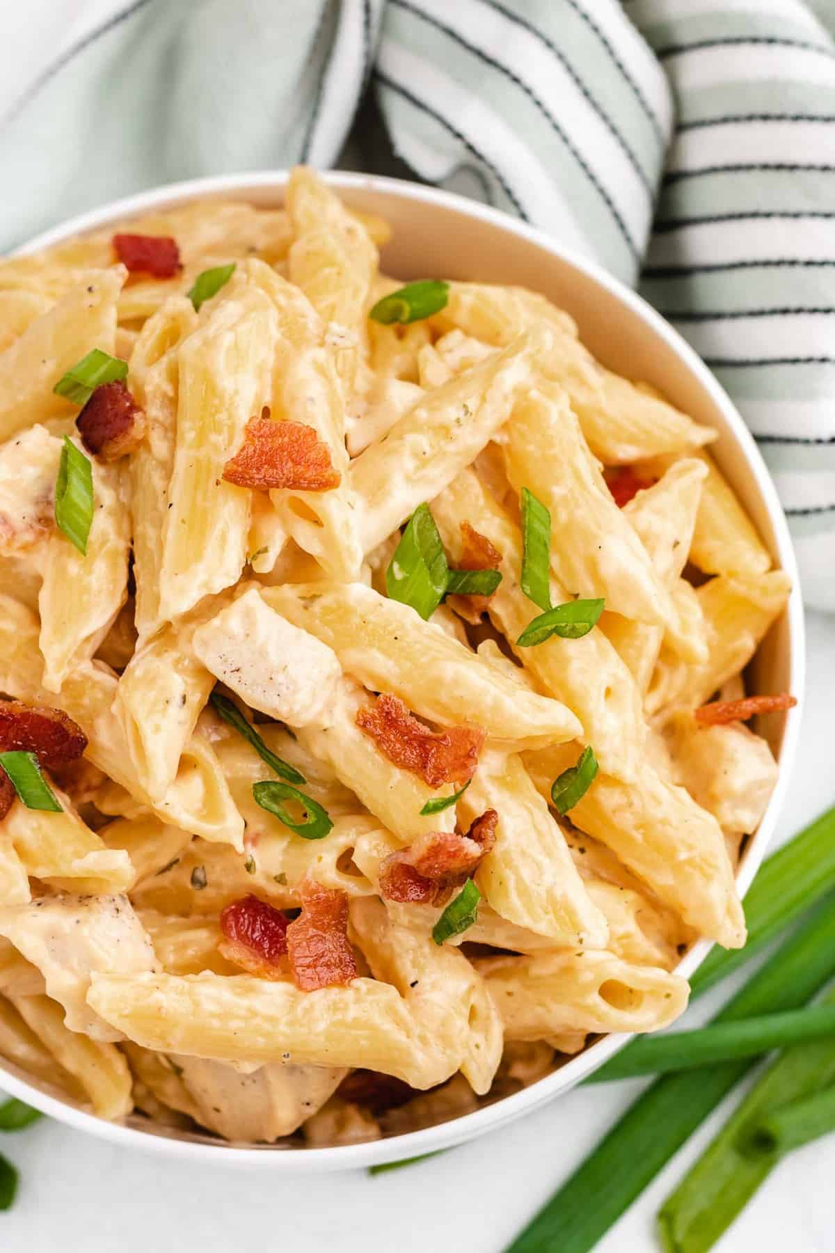 Overhead view of pasta garnished with green onions and bacon.