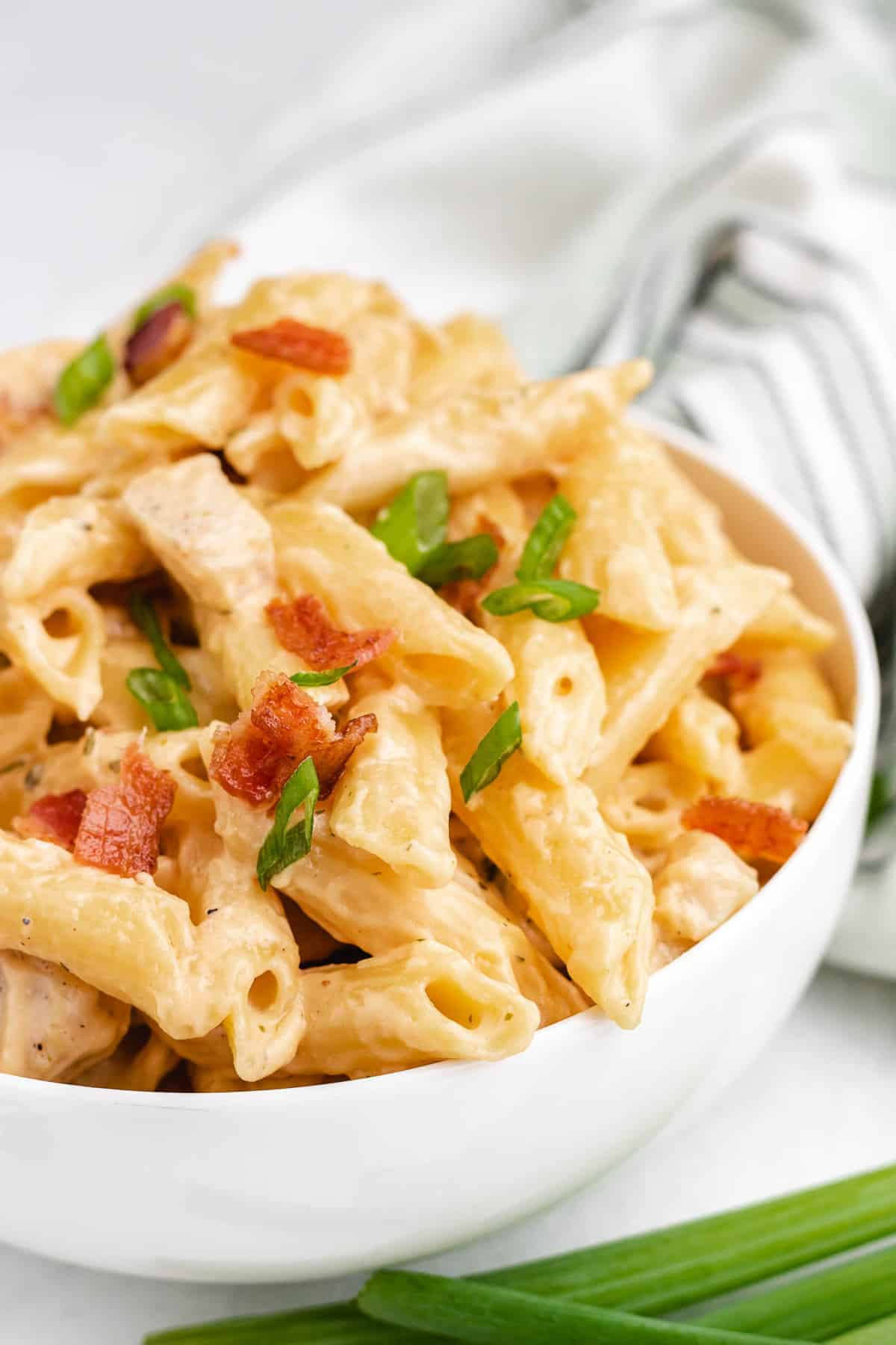 Close up of creamy pasta in a bowl, topped with green onion and bacon.