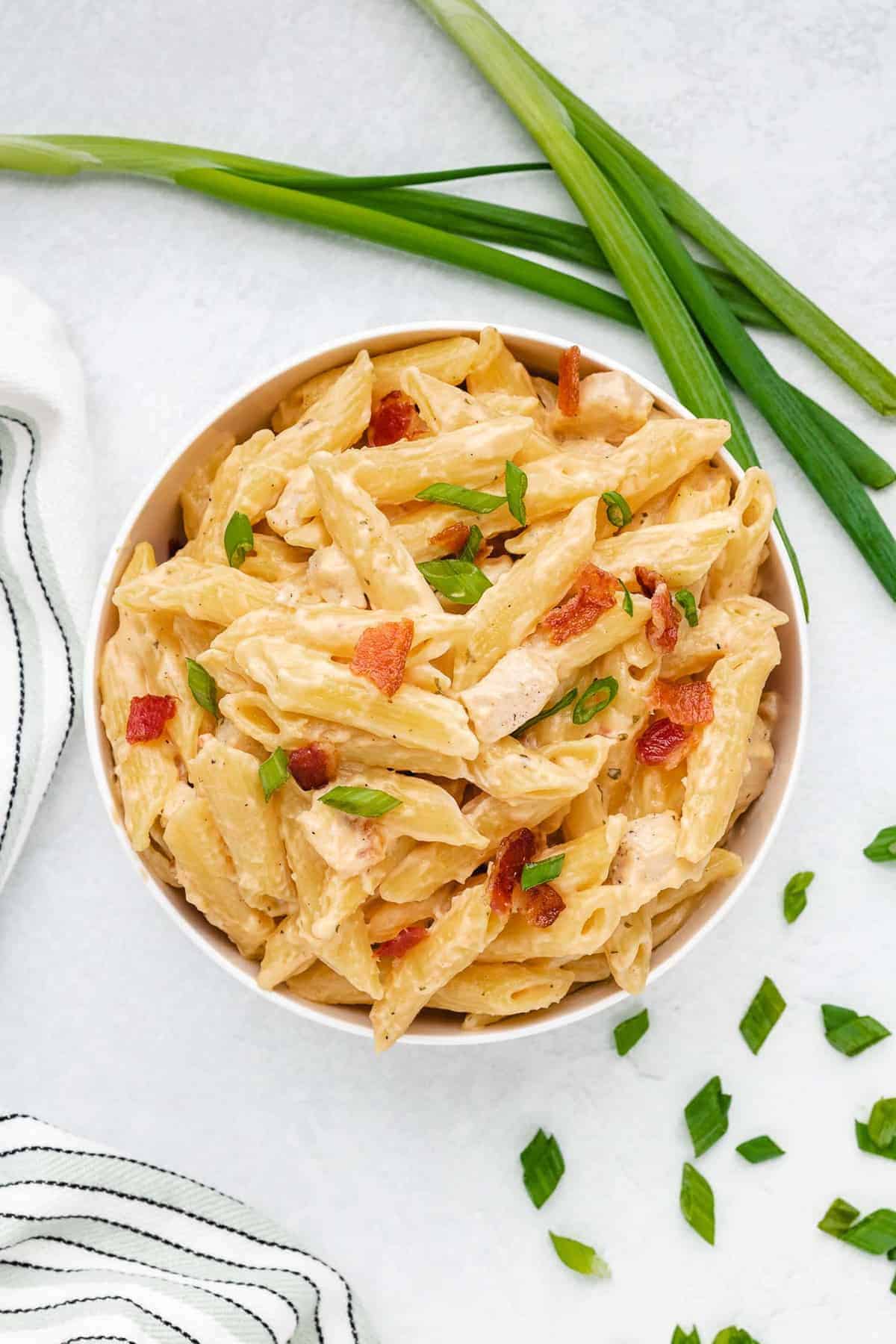 Creamy chicken pasta in a bowl with green onions and bacon.