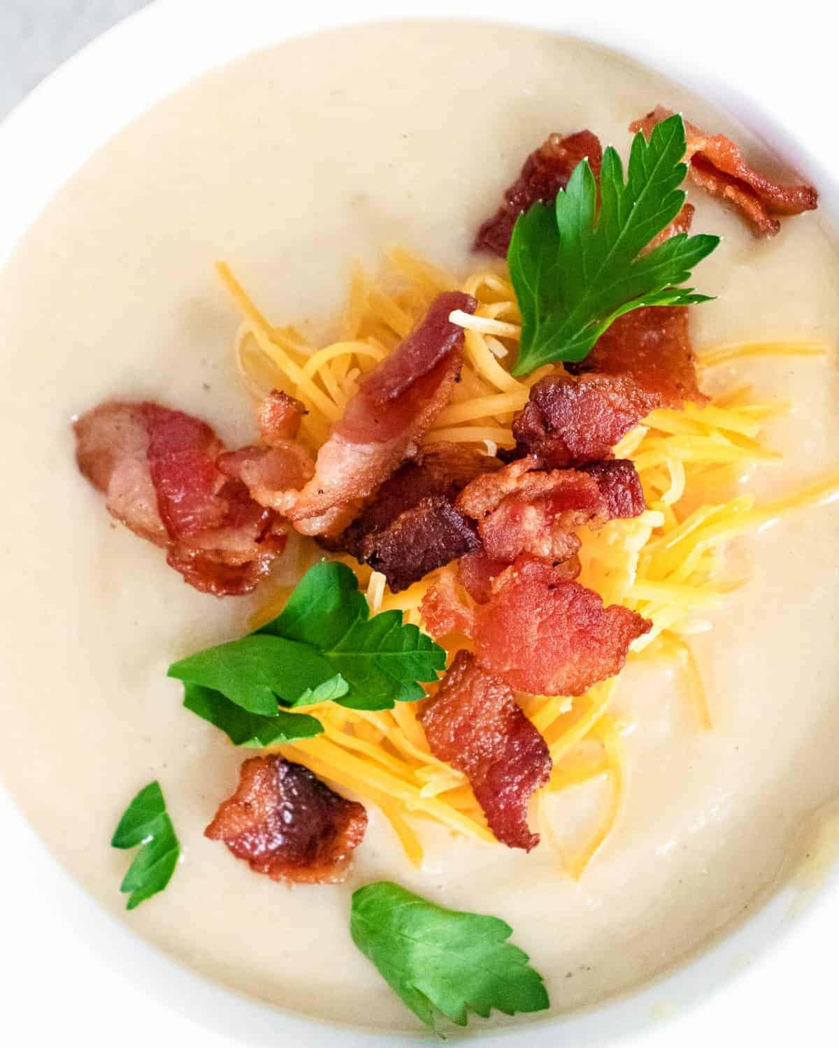 Close up of creamy soup topped with bacon, fresh parsley, and cheddar cheese.