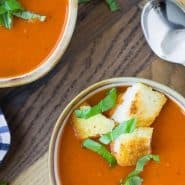 Overhead view of two bowls of tomato soup topped with croutons and fresh basil.