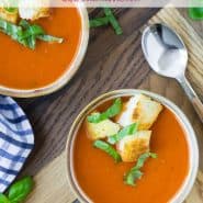 Overhead view of two bowls of tomato soup topped with croutons and fresh basil.