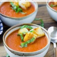 Two bowls of soup made with tomatoes, topped with croutons and basil.