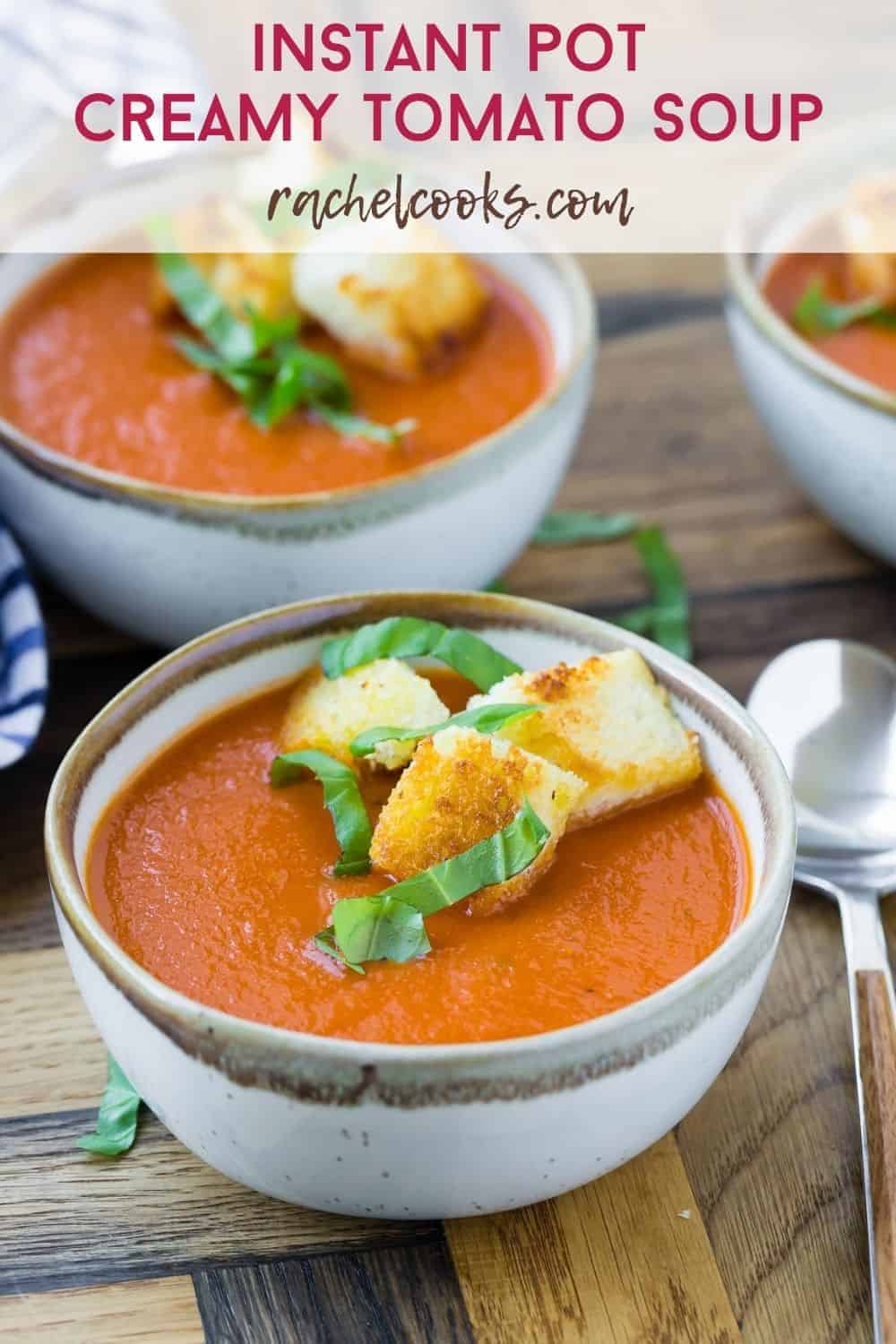 Two bowls of soup made with tomatoes, topped with croutons and basil.