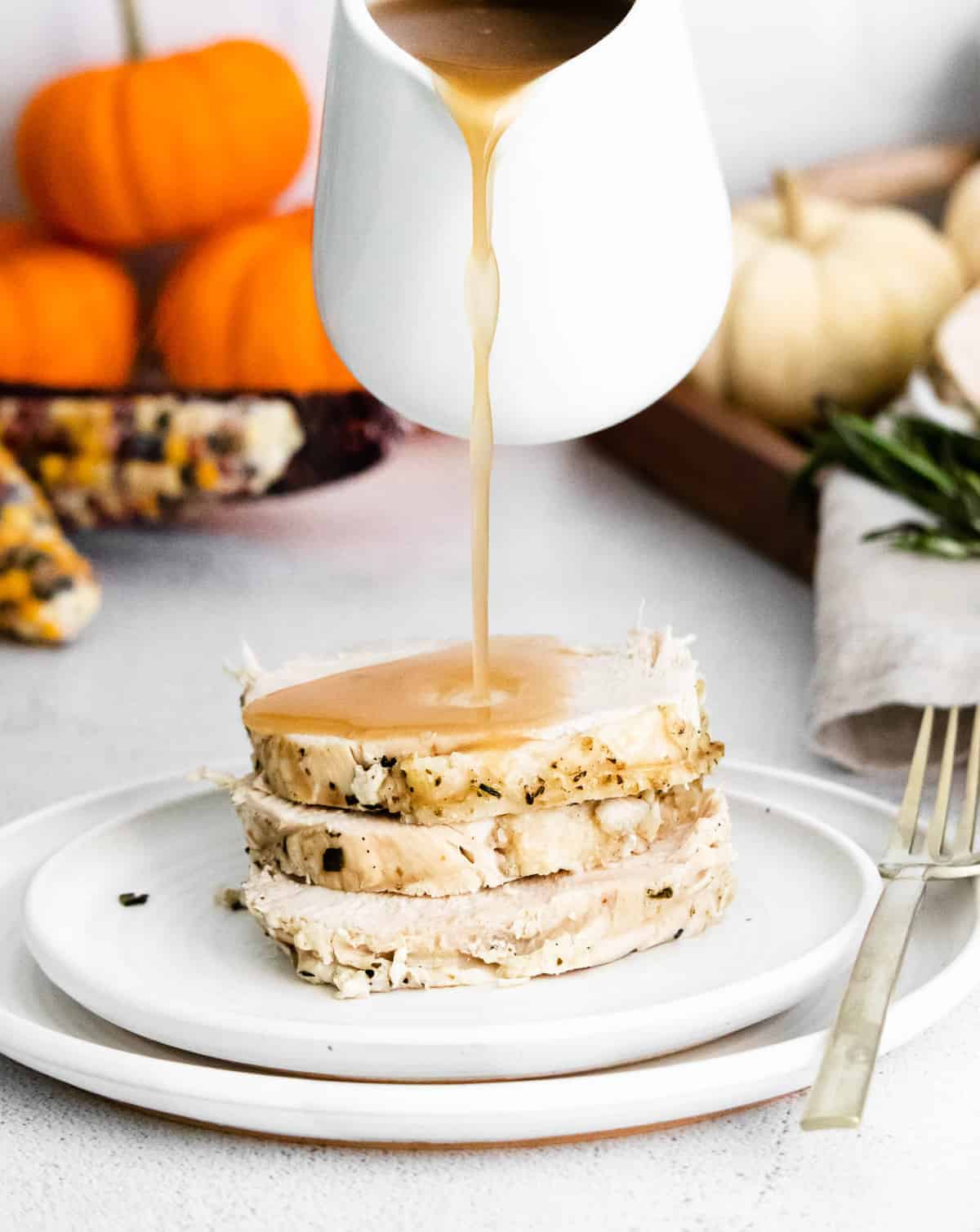 Gravy being poured on a stack of cooked turkey breast.