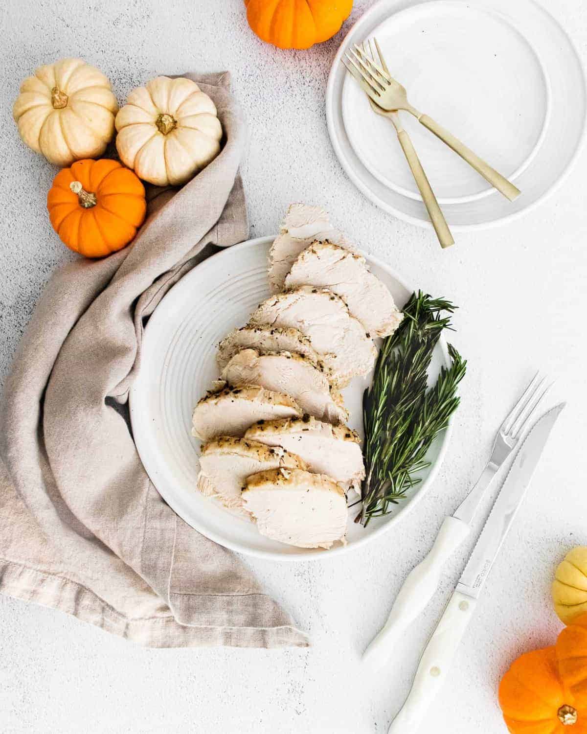 Overhead view of sliced turkey breast with rosemary sprigs and small pumpkins.