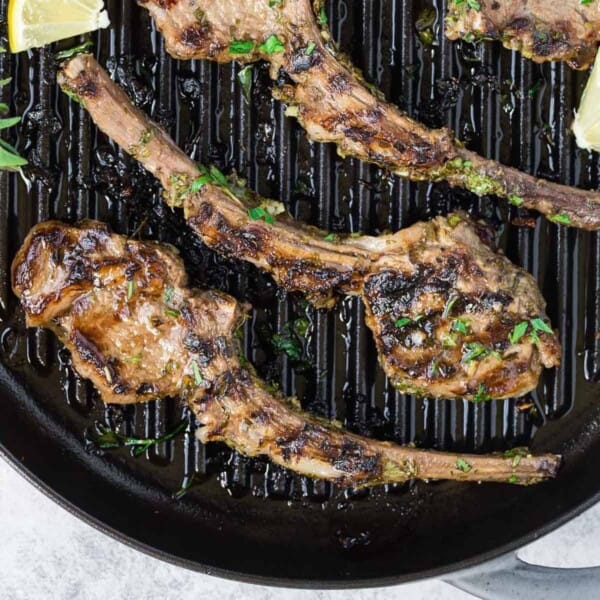 Lamb chops on a grill pan, sprinkled with fresh herbs.