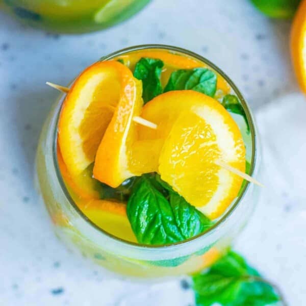 Overhead view of an orange cocktail with fresh orange and mint leaves.