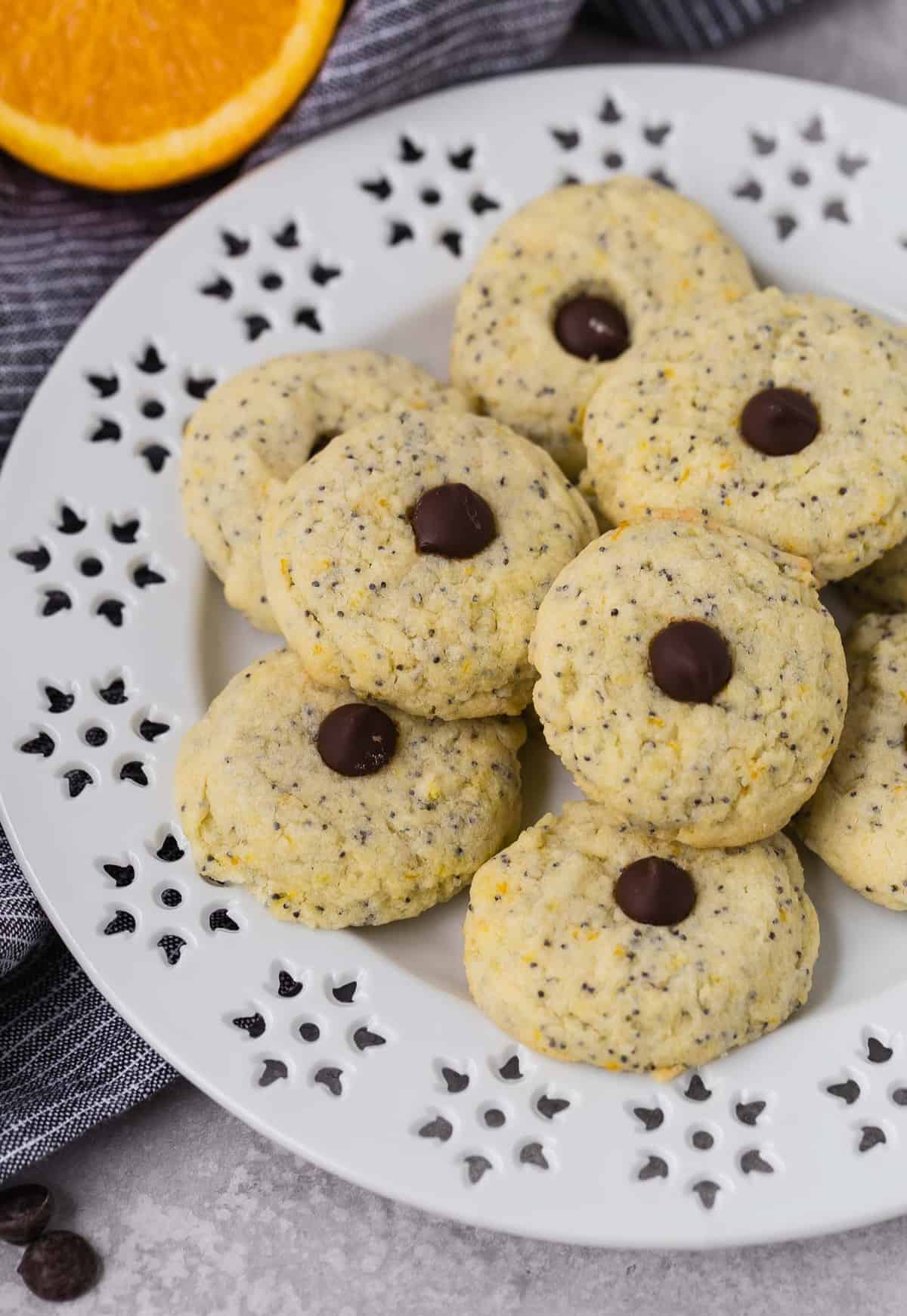 Cookies flecked with poppy seeds and orange zest on a white plate. Each cookie is topped with a chocolate chip.