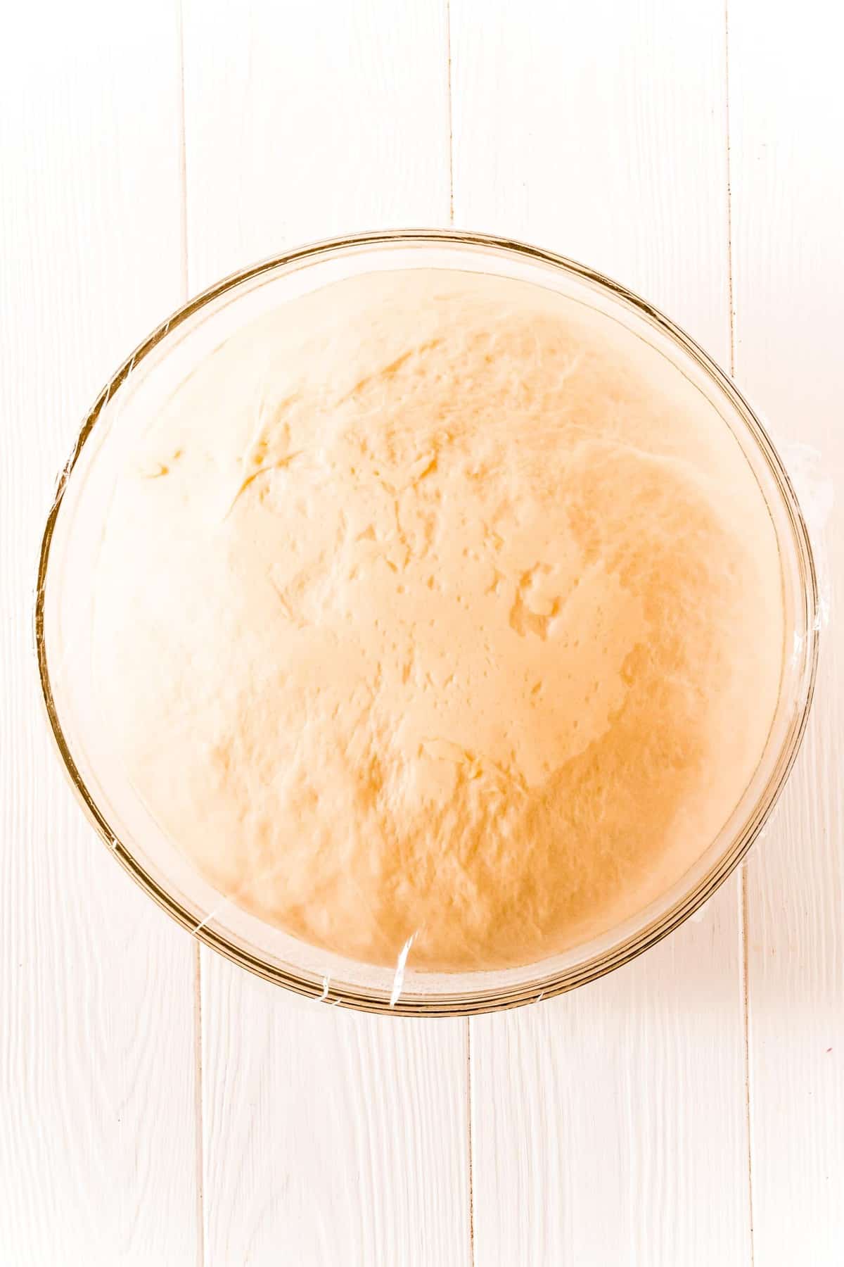 Dough for rolls in a glass bowl, doubled in size after first rise.