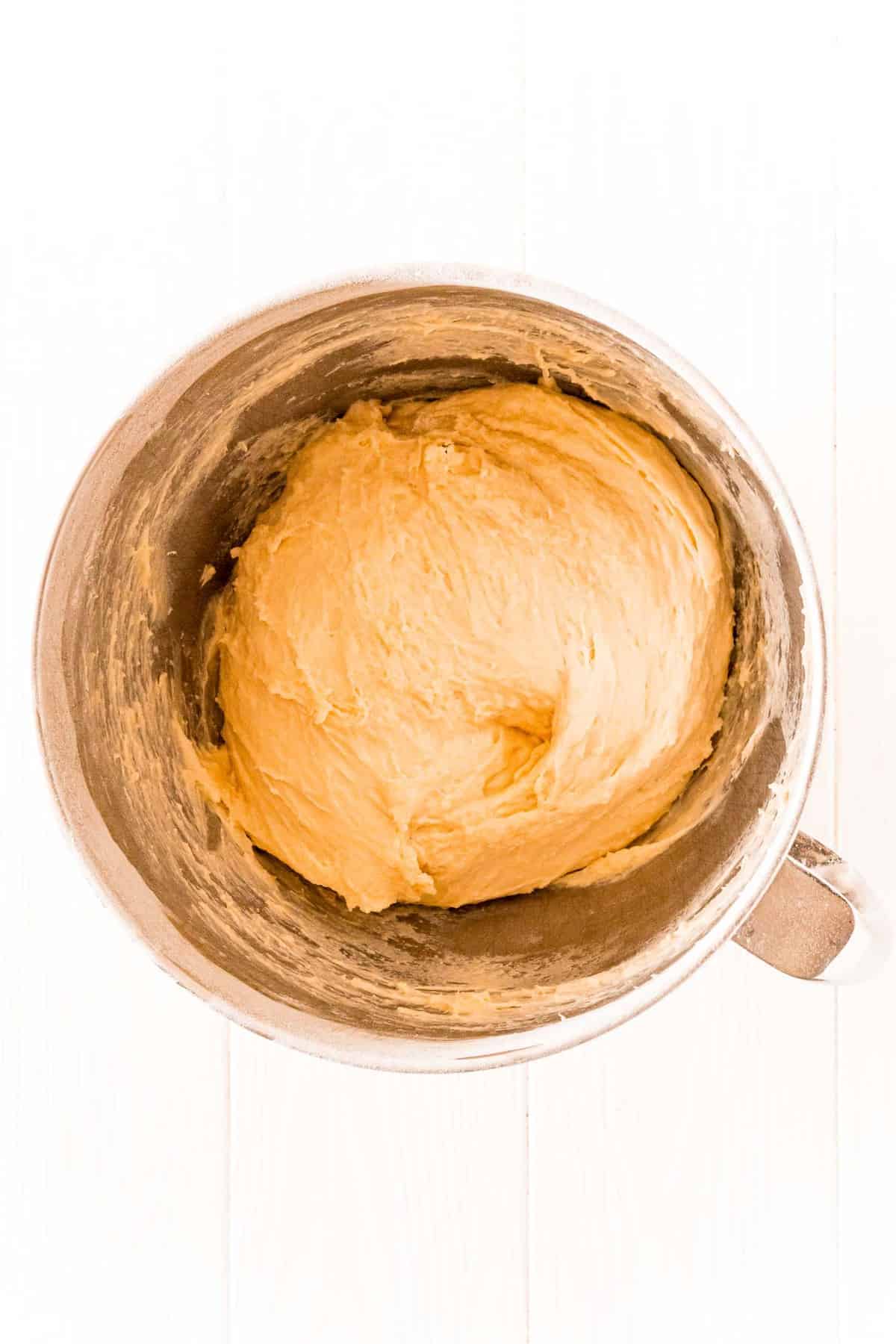 Bread dough in a metal mixing bowl on a white background.