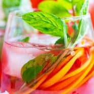 Brightly colored red drink with pomegranate arils, citrus slices, and fresh mint. Text overlay reads "sparkling pomegranate punch"