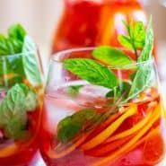 Brightly colored red drink with pomegranate arils, citrus slices, and fresh mint. Text overlay reads "sparkling pomegranate punch"