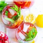 Brightly colored red drink with pomegranate arils, citrus slices, and fresh mint. Text overlay reads "sparkling pomegranate punch"