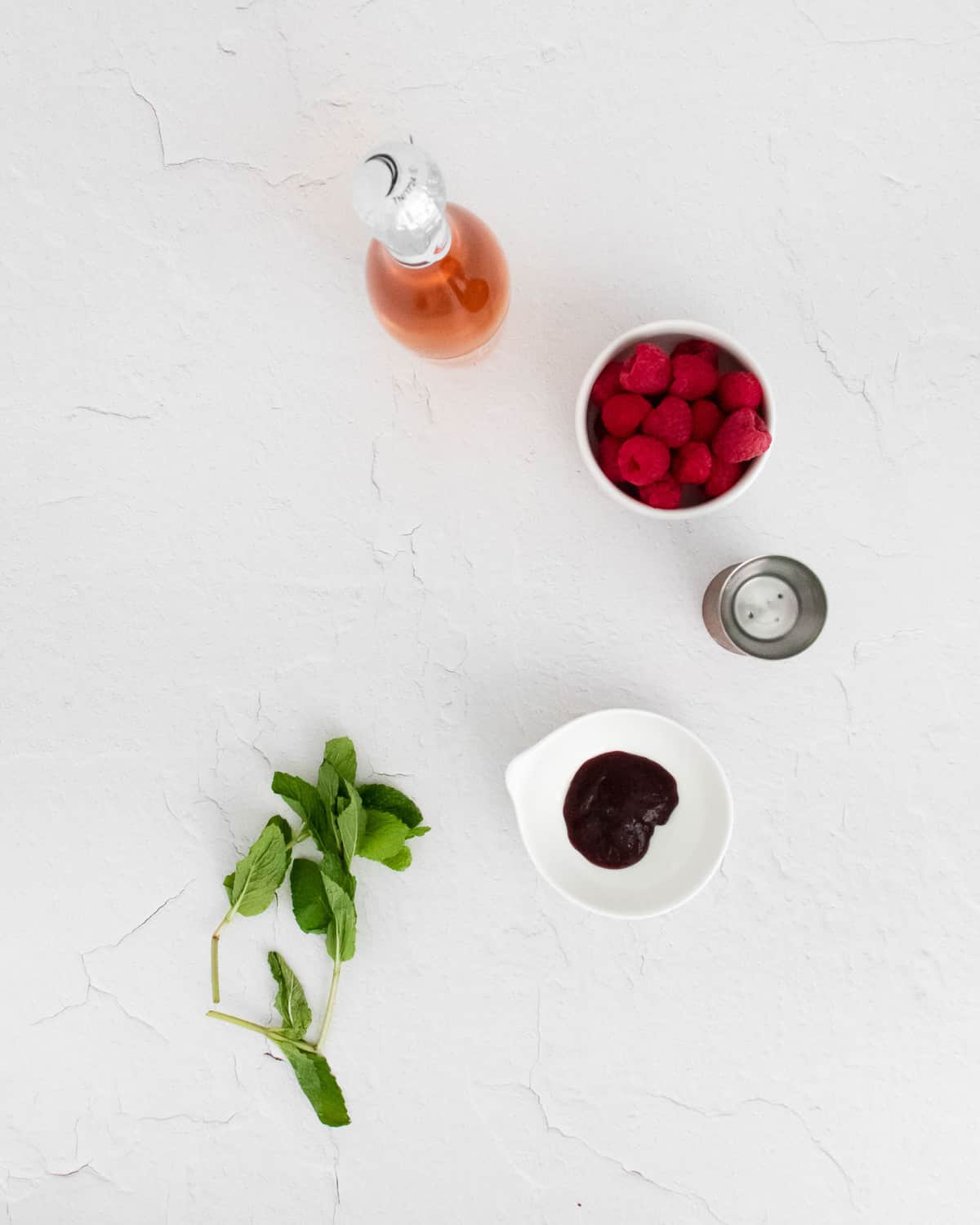 Overhead view of mint, jam, vodka, raspberries, and rose.