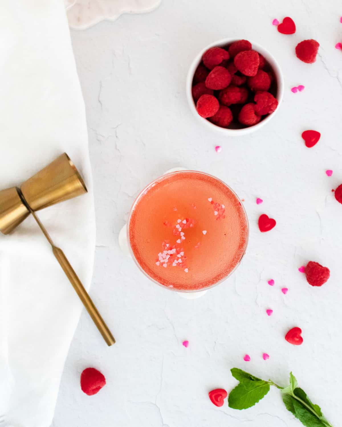 Overhead view of a light pink cocktail, raspberries scattered around.