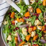 Colorful salad made with arugula, roasted cauliflower, sweet potatoes, shallots, and pomegranate seeds