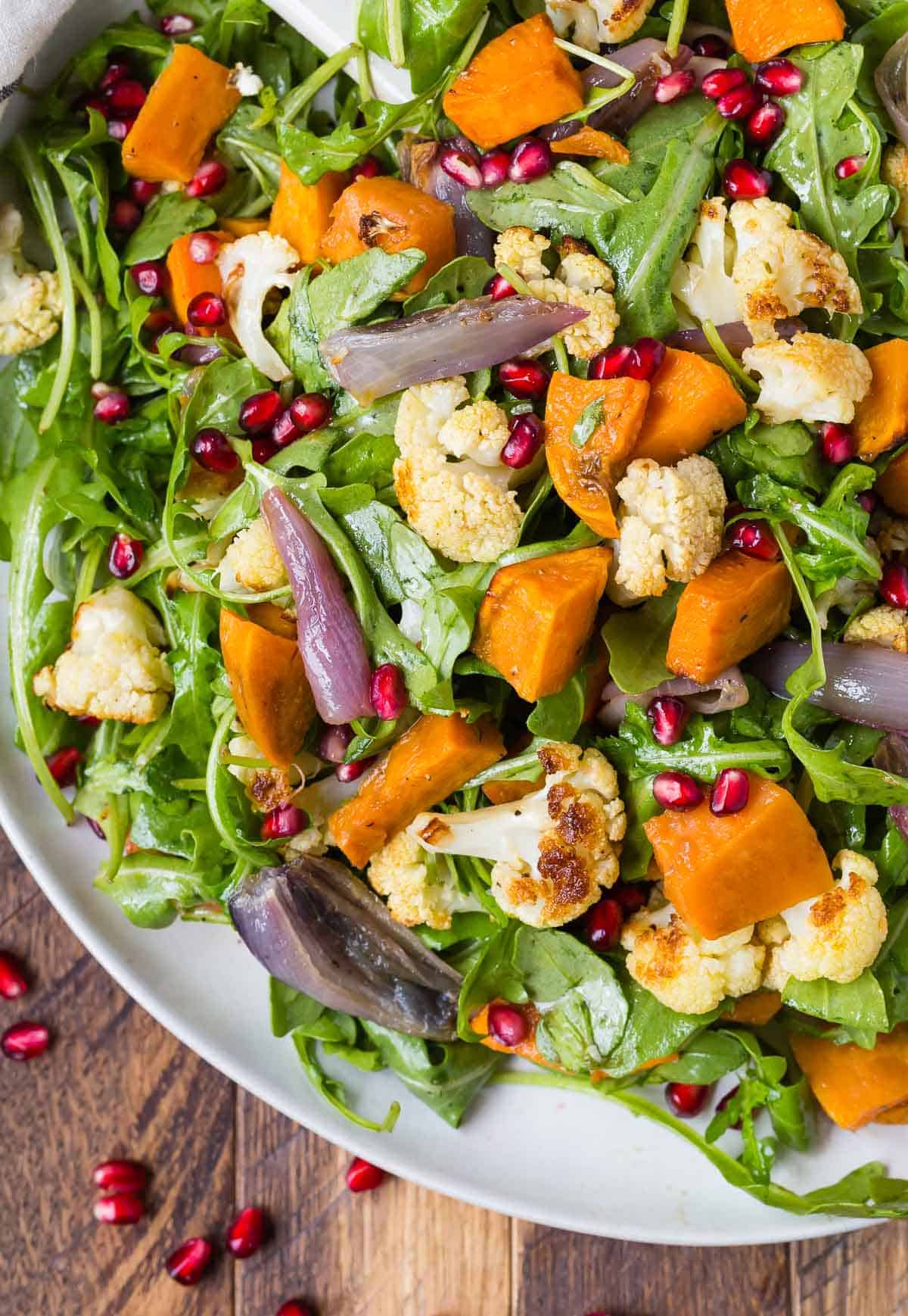 Arugula on a large white platter, topped with roasted cauliflower and roasted sweet potatoes.