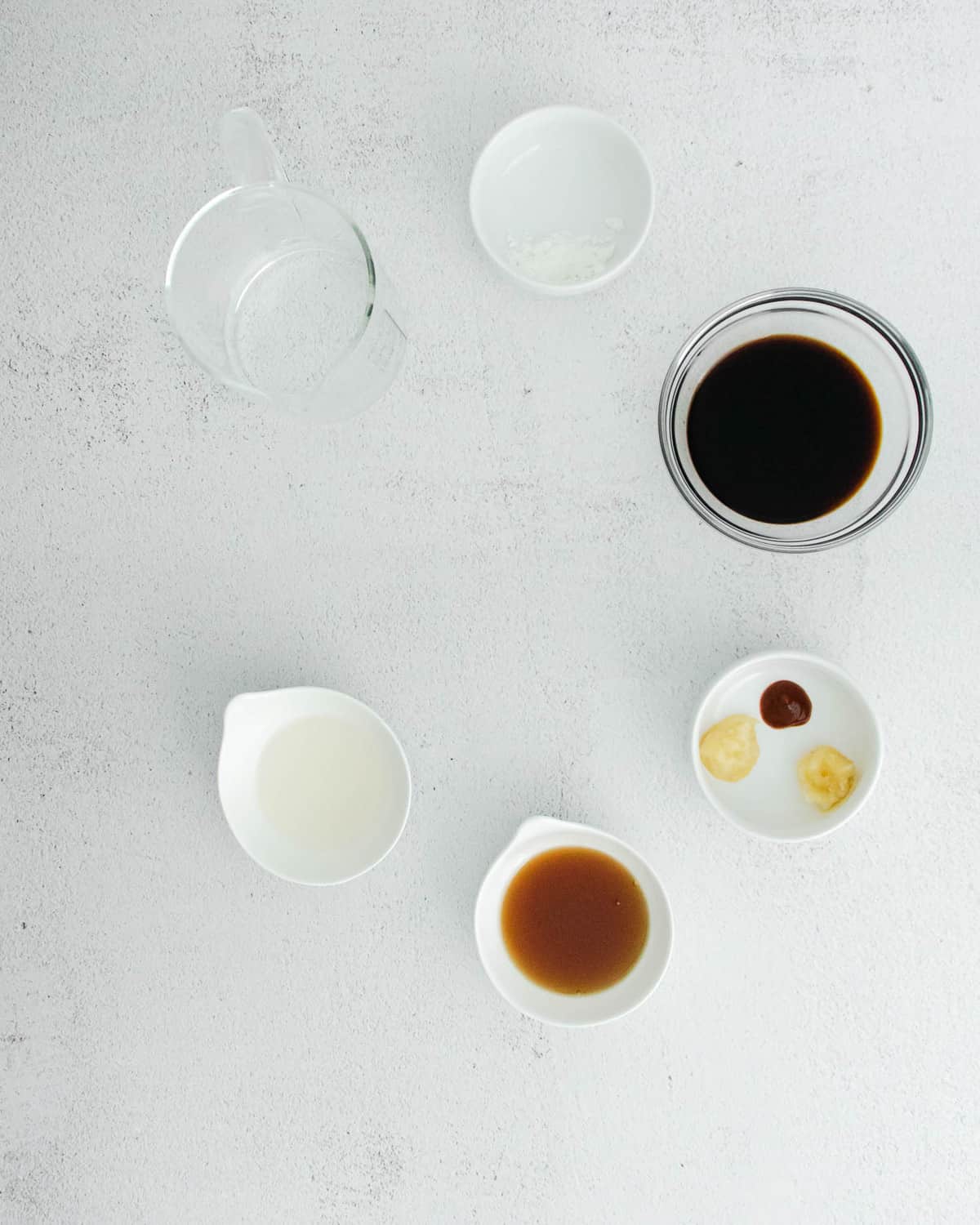 Sauce ingredients in small bowls on a light grey surface.