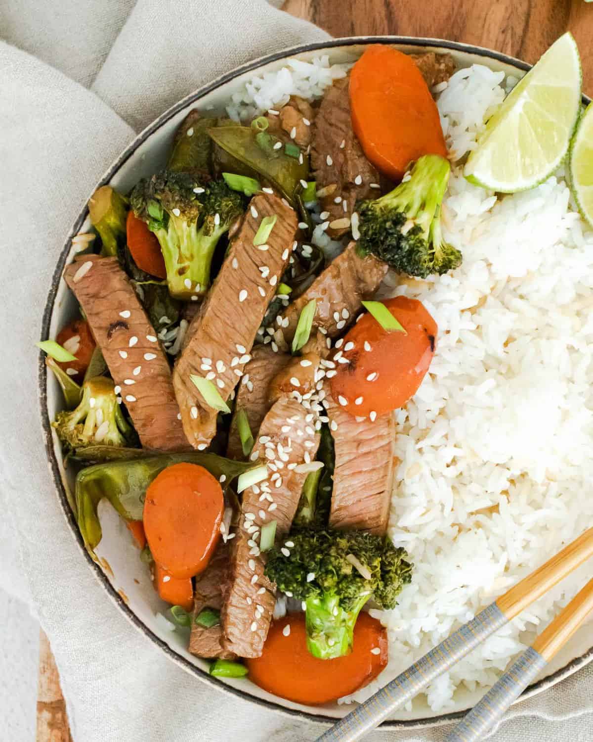 Cooked beef and vegetables in a bowl with rice, topped with sesame seeds.