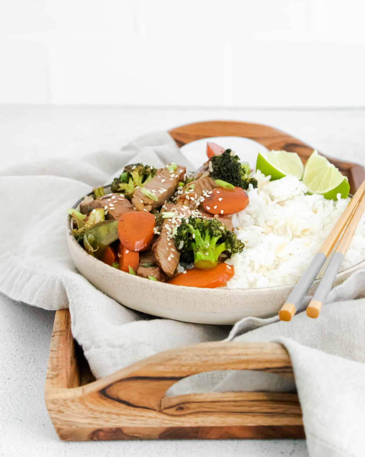 Bowl of rice, vegetables, steak, and sesame seeds on a tray with chopsticks.
