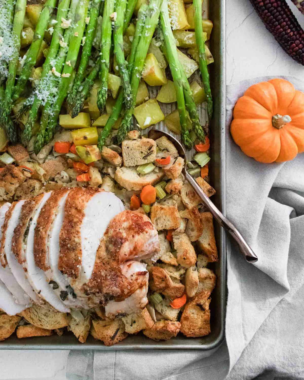 A sheet pan with a turkey breast, sourdough dressing, roasted potatoes, and asparagus.