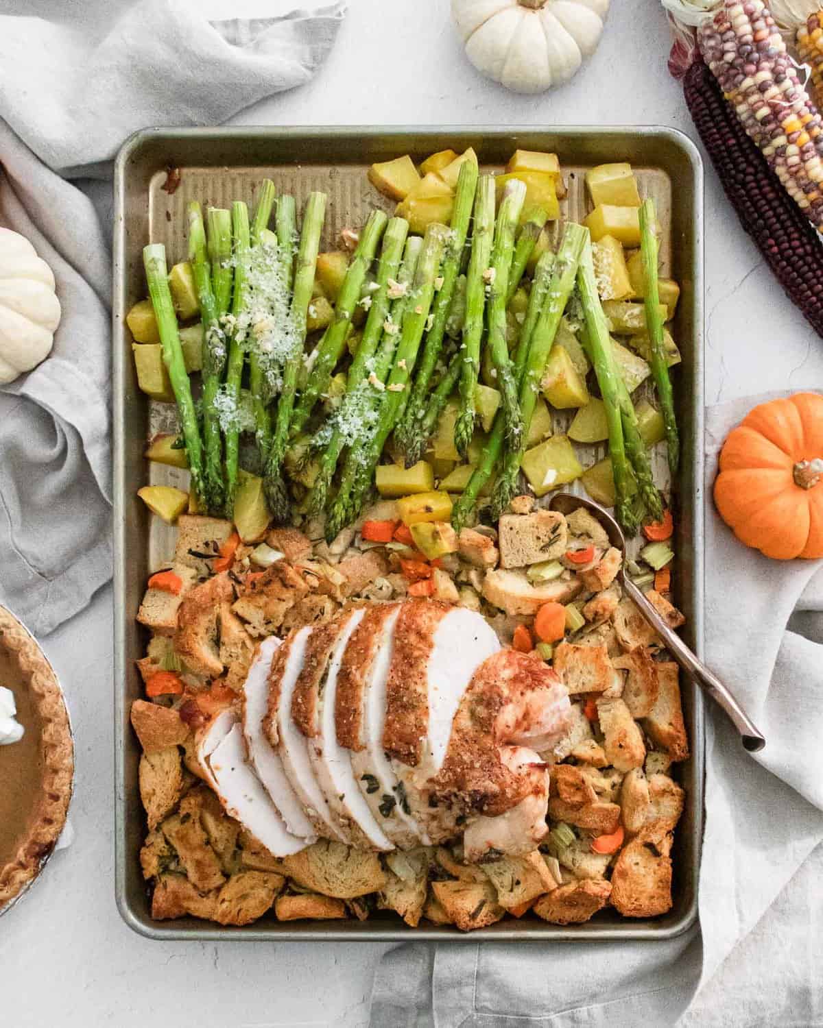 Overhead view of a sheet pan thanksgiving dinner with turkey, stuffing, potatoes, and asparagus.